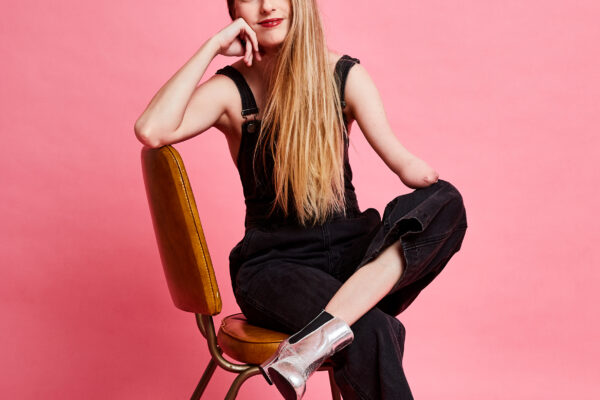 Madeline Stewart leaning in a chair against a pink background.