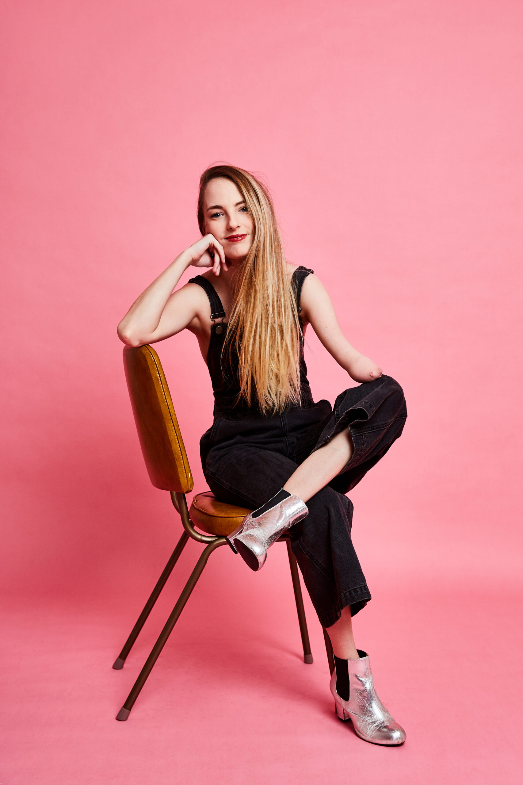 Madeline Stewart leaning in a chair against a pink background.