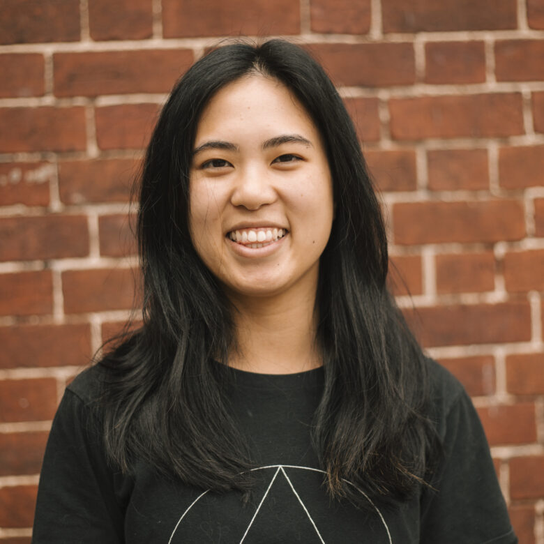 A headshot of Ash Hem in front of a brick wall