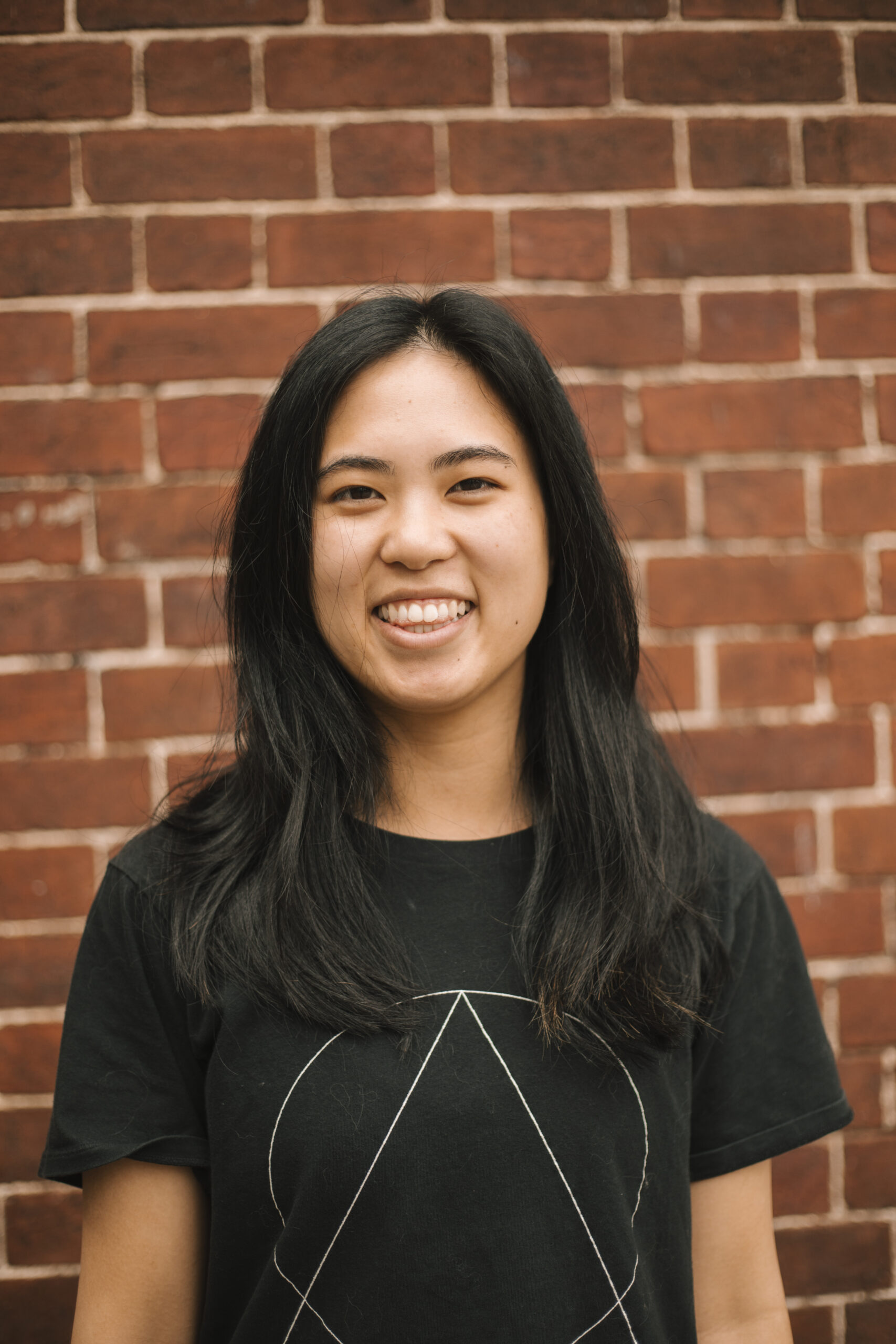 A headshot of Ash Hem in front of a brick wall