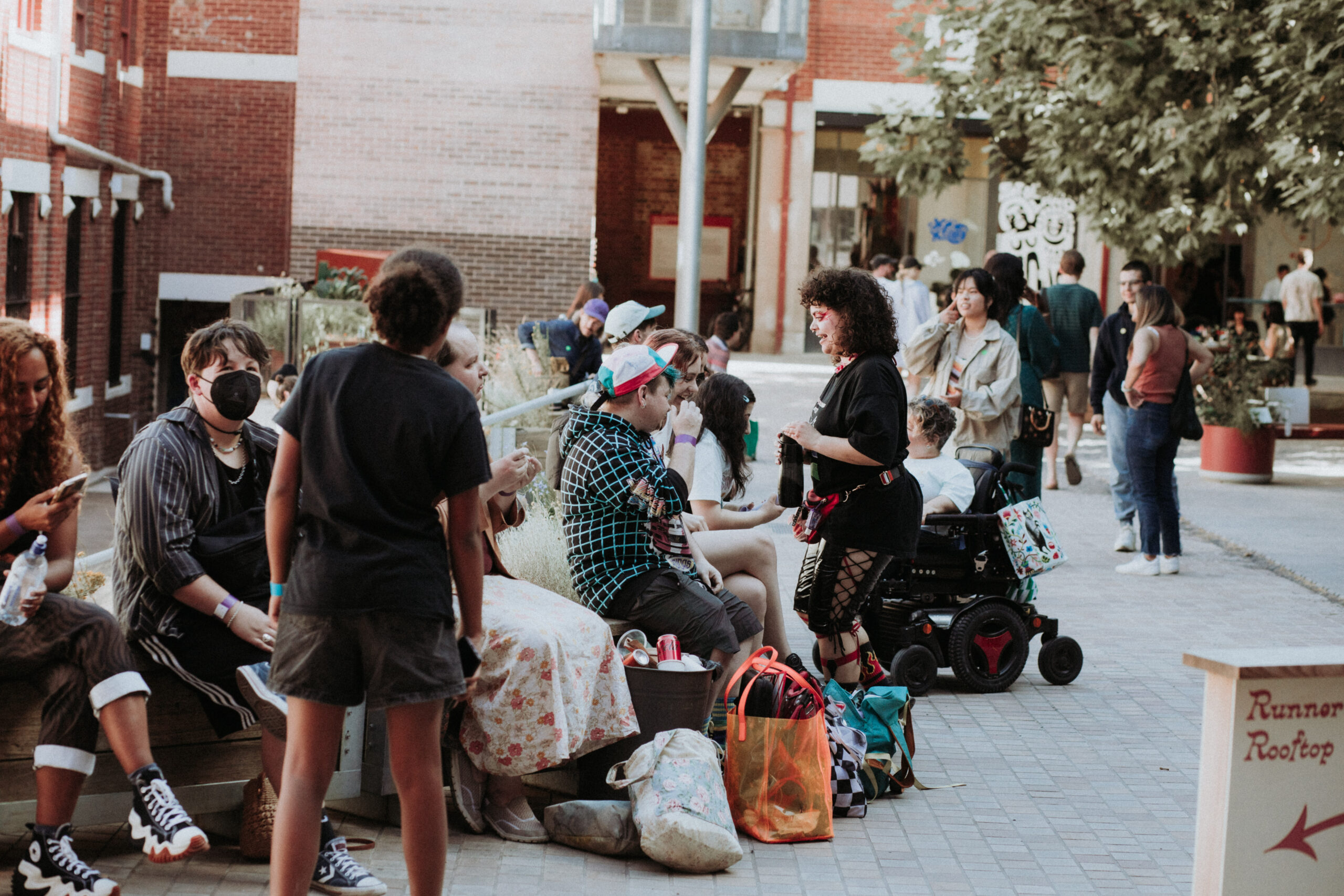 A group of people relaxing and chatting sitting and standing, pictured in a courtyard.