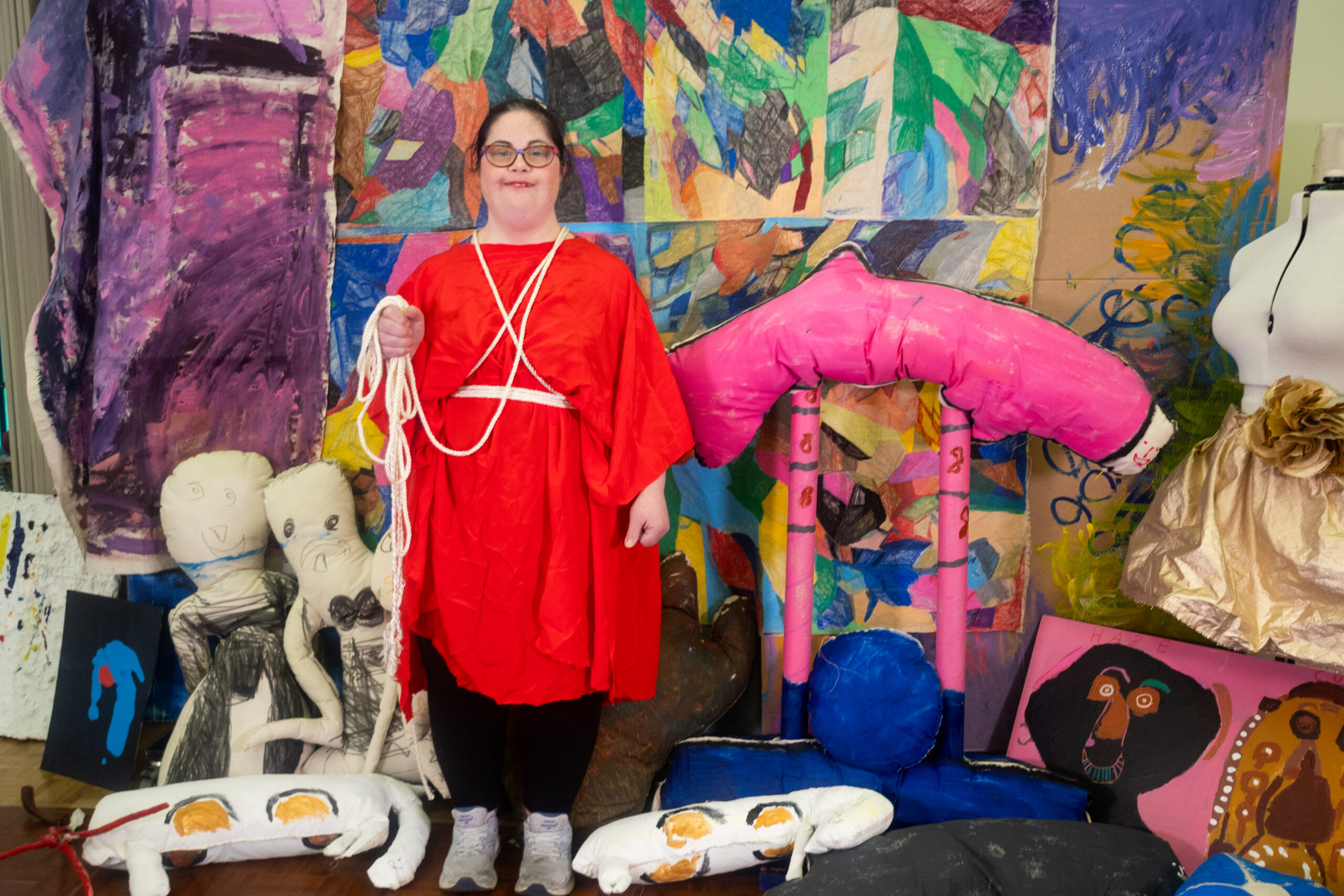 Woman dressed in red standing amongst colourful artworks.