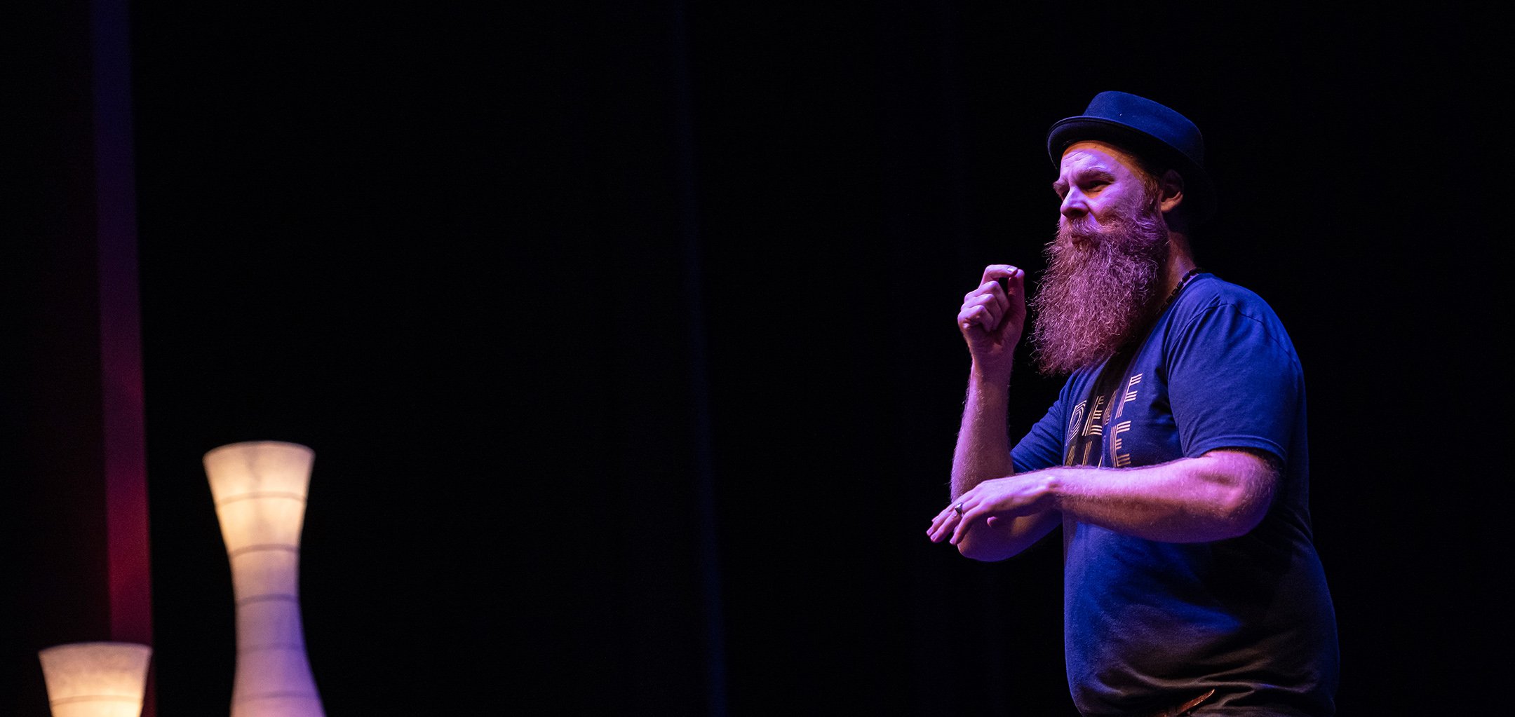 Ramas McRae in performance in a dark theatre space, with two lights to the left of the image.