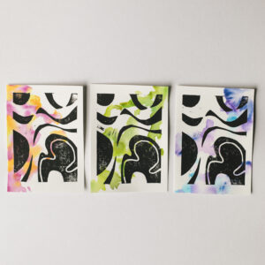 Set of 3 linocuts with colourful watercolour backgrounds. The colours are pink and orange on the left print, green in centre, and blue and purple on the right.