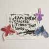 Linocut print in black ink of a text saying ‘I am every cracked thing that sings’. There is a red watercolour flower on the left side of the frame. There are purple and dark blue flowers on the right side.