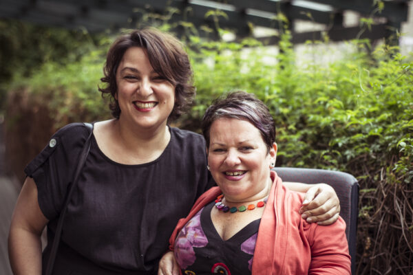 Two people smiling in front of some outdoor greenery.